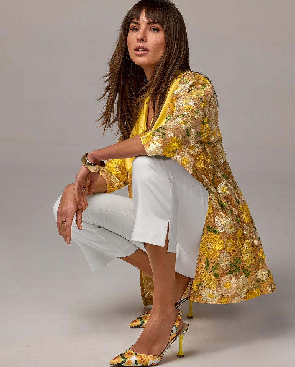 Model is wearing yellow floral jacket with white pants and yellow floral heels